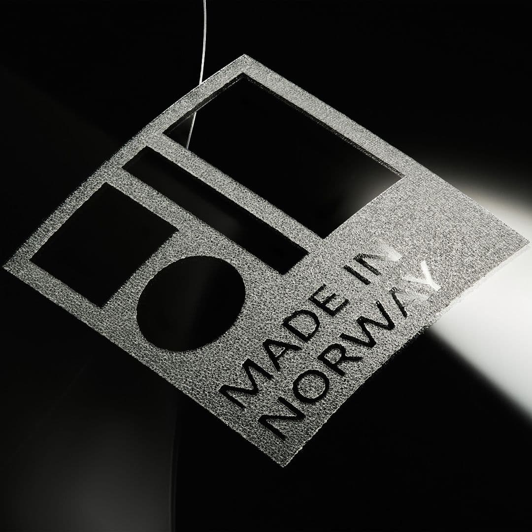 En lapp med Made in Norway-merket, hengende foran en mørk bakgrunn.