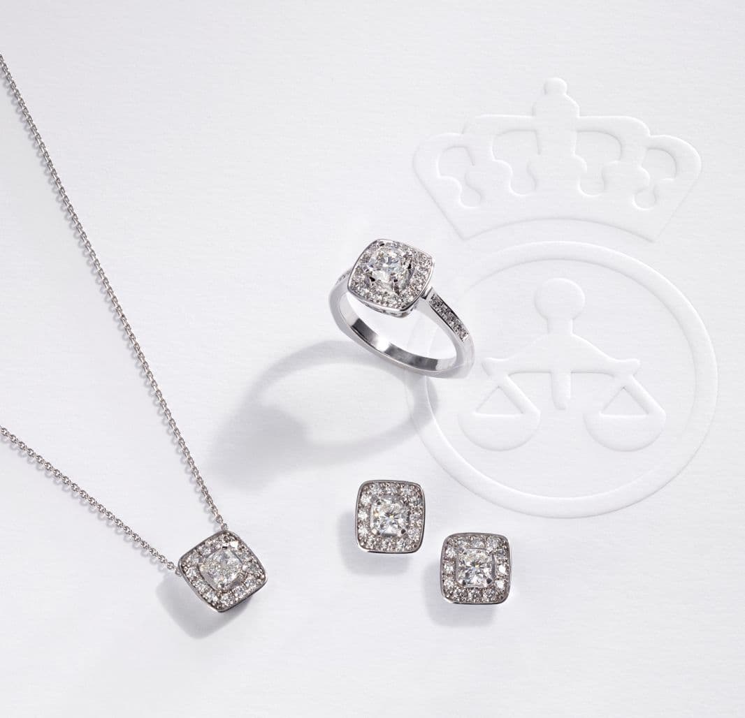 Flere diamantsmykker ligger på hvit bakgrunn. Et kjede, en ring og et par øredobber.