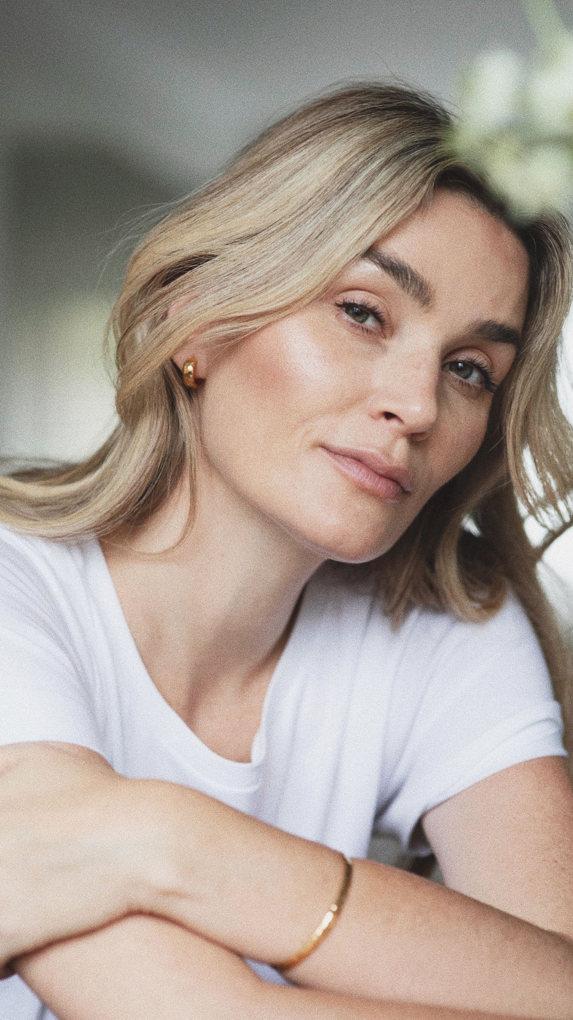Portrett av Camilla Pihl med hendene hvilende over armene. Hun er iført en hvit t-skjorte, et gullarmbånd og små øreringer i gull.